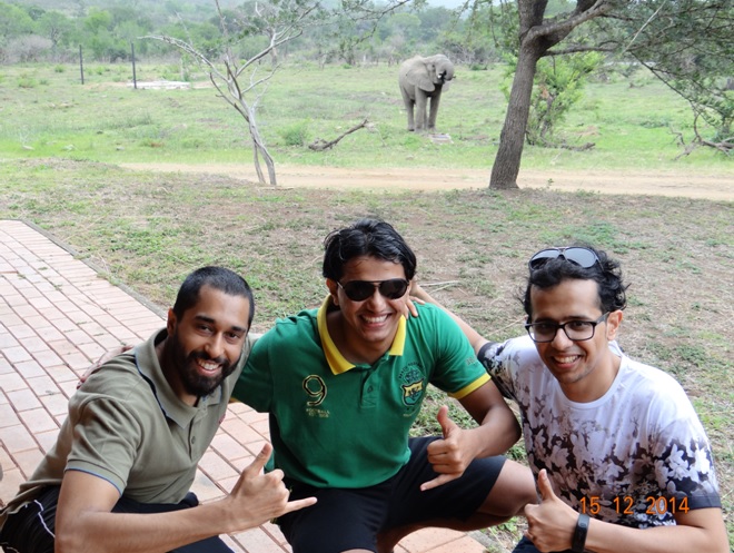 Hussein, Achmed and Fahad posing with a male Elephant drinking water behind them
